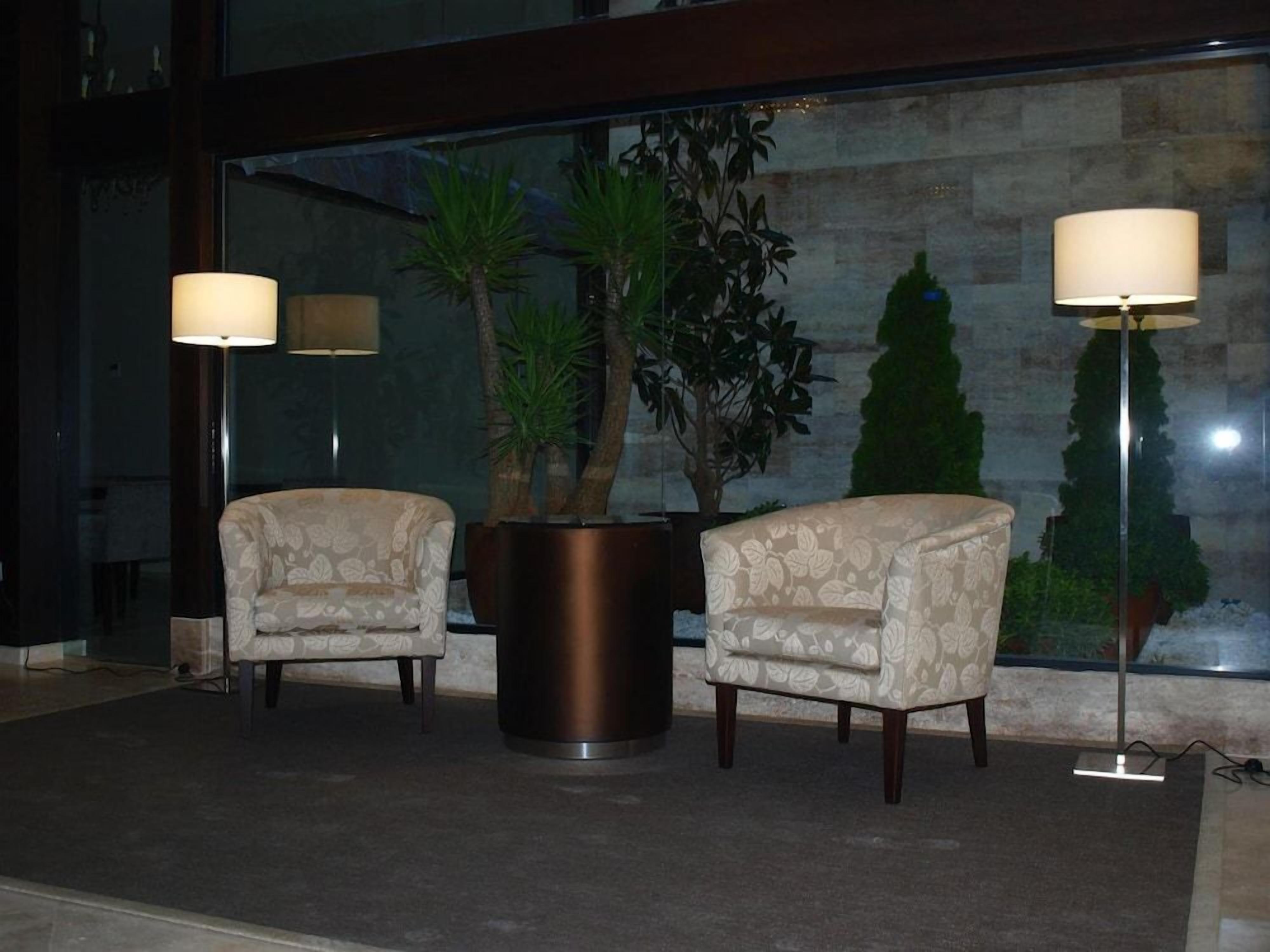 A lobby with two armchairs, a potted plant, and a floor lamp.