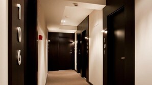 A hotel hallway with numbered doors, a carpeted floor, and a ceiling light fixture. - Hotel Paloma (Tomelloso)
