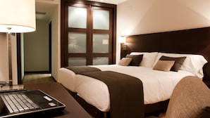 A hotel room with a bed, bedside lamps, a desk with a laptop, and a door with frosted glass panels. - Hotel Paloma (Tomelloso)