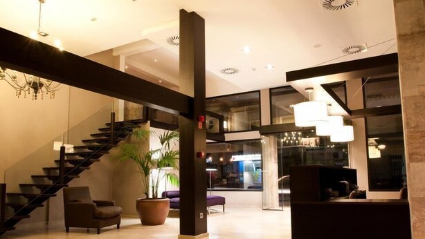 A modern lobby with a staircase, seating area, and a reception desk. - Hotel Paloma (Tomelloso)