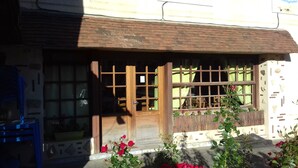A building with a wooden door and windows, surrounded by a garden with red flowers. - Auberge Des Pilotis (Beauvoir-en-Lyons)