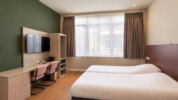 Een hotelkamer met een bed, een bureau met stoel, een televisie en een kledingkast.