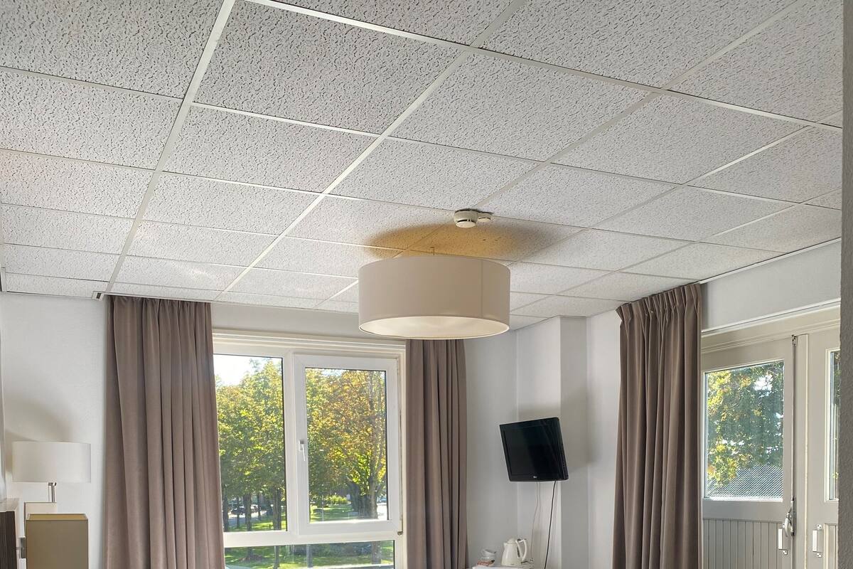 Een hotelkamer met een bed, een bureau, een stoel, een televisie en een raam met gordijnen.