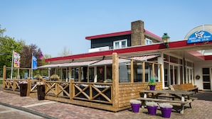 Un espace extérieur aménagé avec des bancs et des plantes en pot, le tout en bois, sous un ciel bleu dégagé, avec une enseigne d’hôtel.