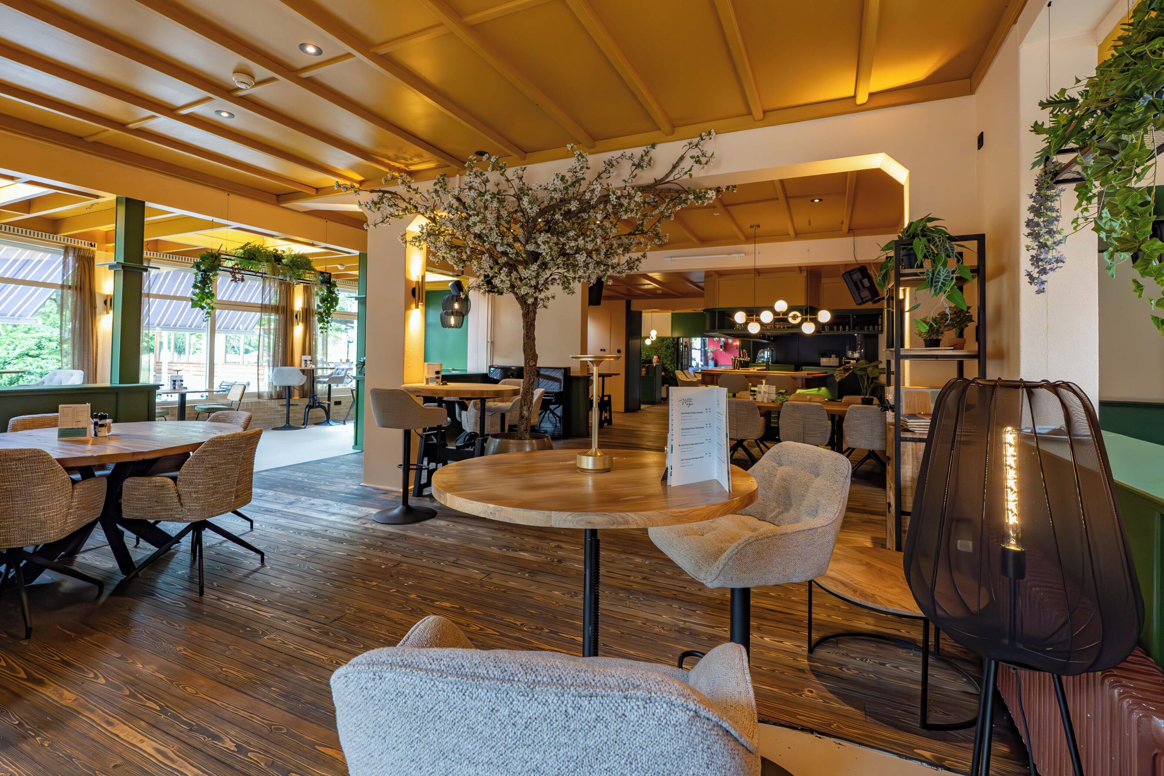 Een restaurantinterieur met houten vloeren, ronde tafels en stoelen.