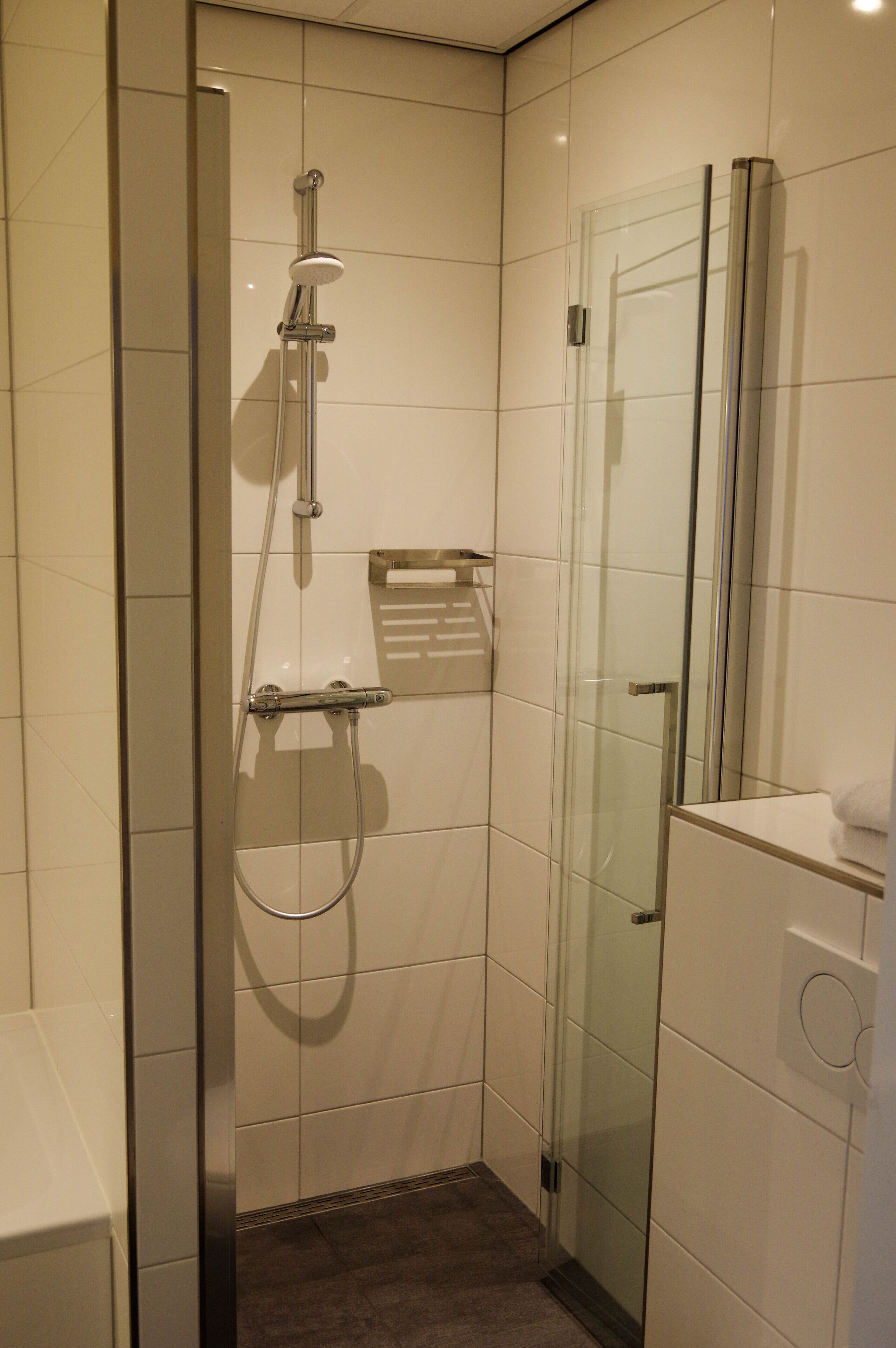A modern bathroom with a glass-enclosed shower, a glass door, and a white tiled wall.