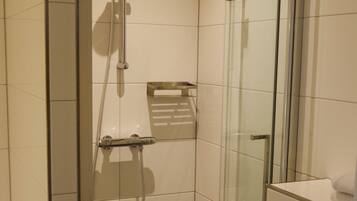 A modern bathroom with a glass-enclosed shower, a glass door, and a white tiled wall.