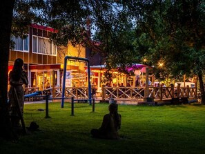 Een buitenzitgedeelte met tafels en stoelen, een houten hek en een gebouw met verlichte ramen op de achtergrond.
