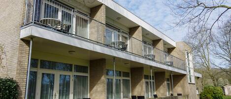 A multi-story building with a balcony on the second floor, large windows, and a brick facade.
