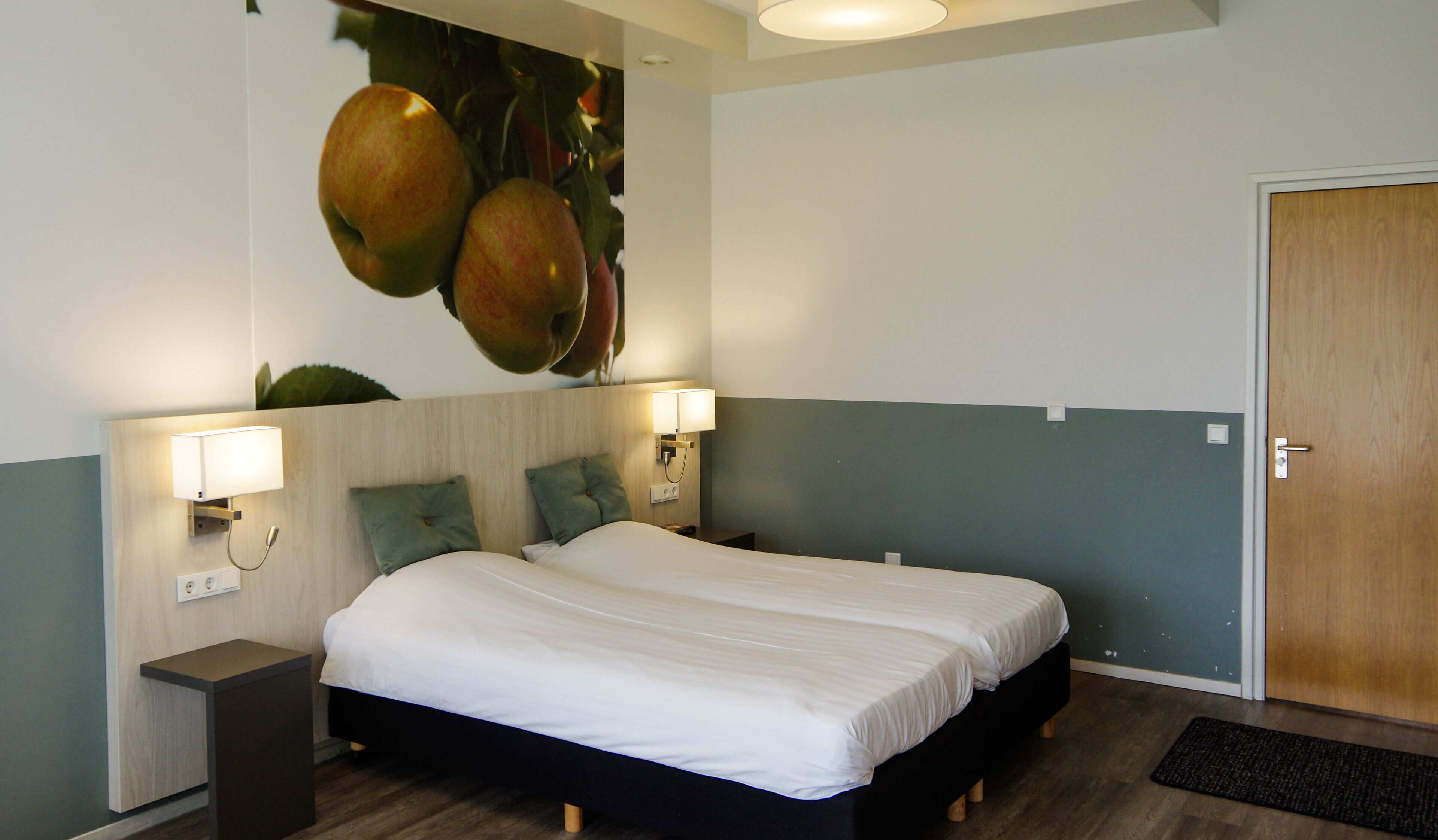 A hotel room with a bed, two bedside tables, a wall-mounted lamp, and a door.