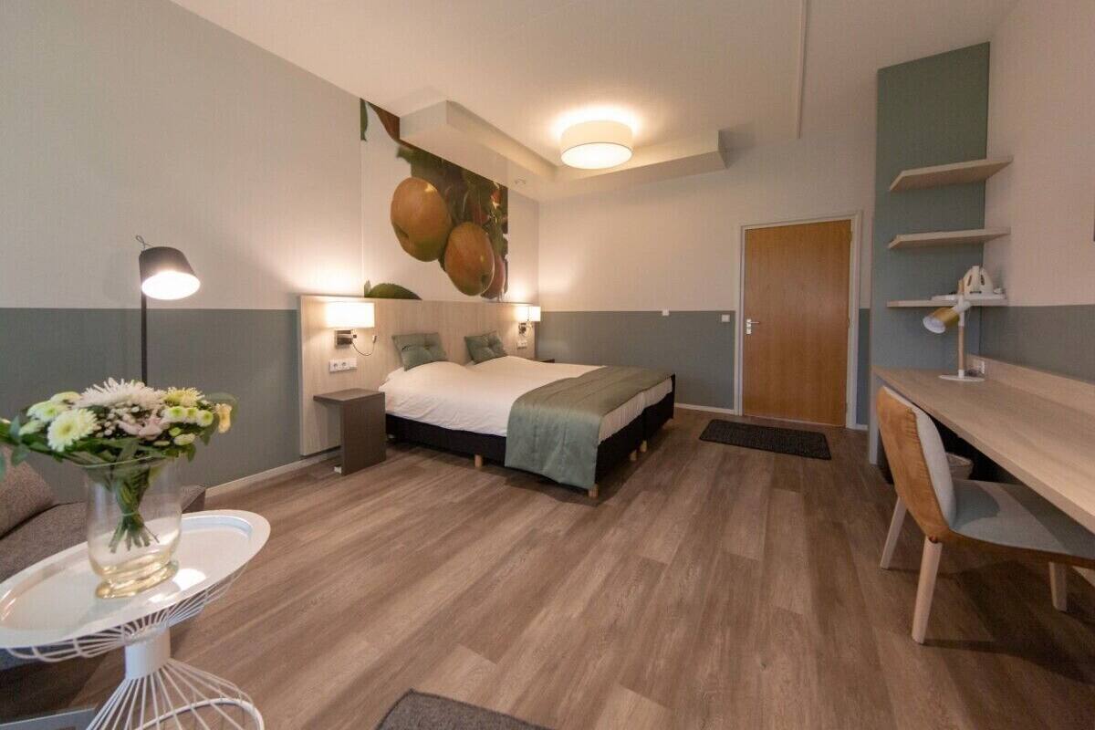 Een slaapkamer met een bed, nachtkastjes, een bureau en een stoel. Er is een deur en een wandplank.