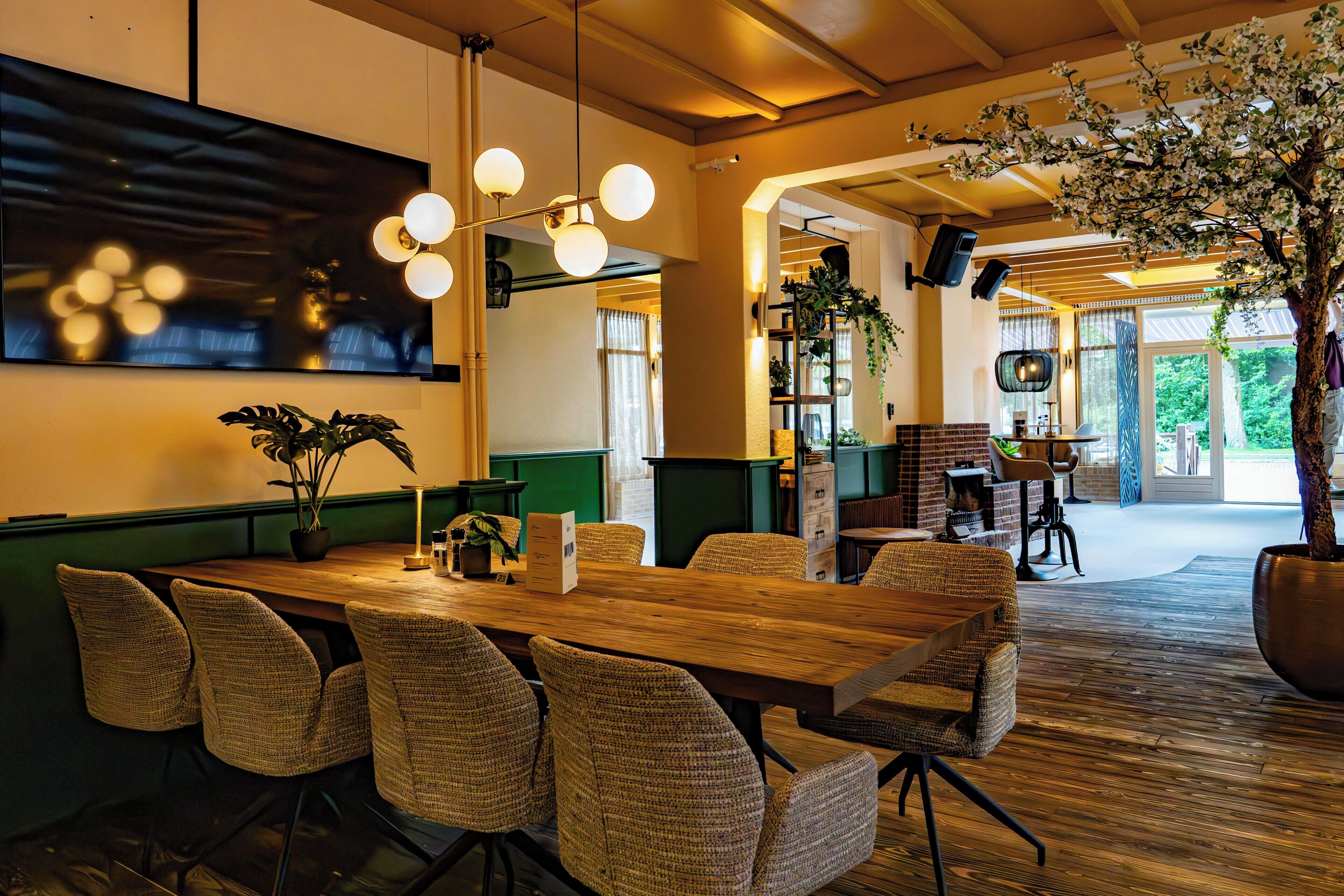 A spacious room with a long wooden table, wicker chairs, and a large potted plant.