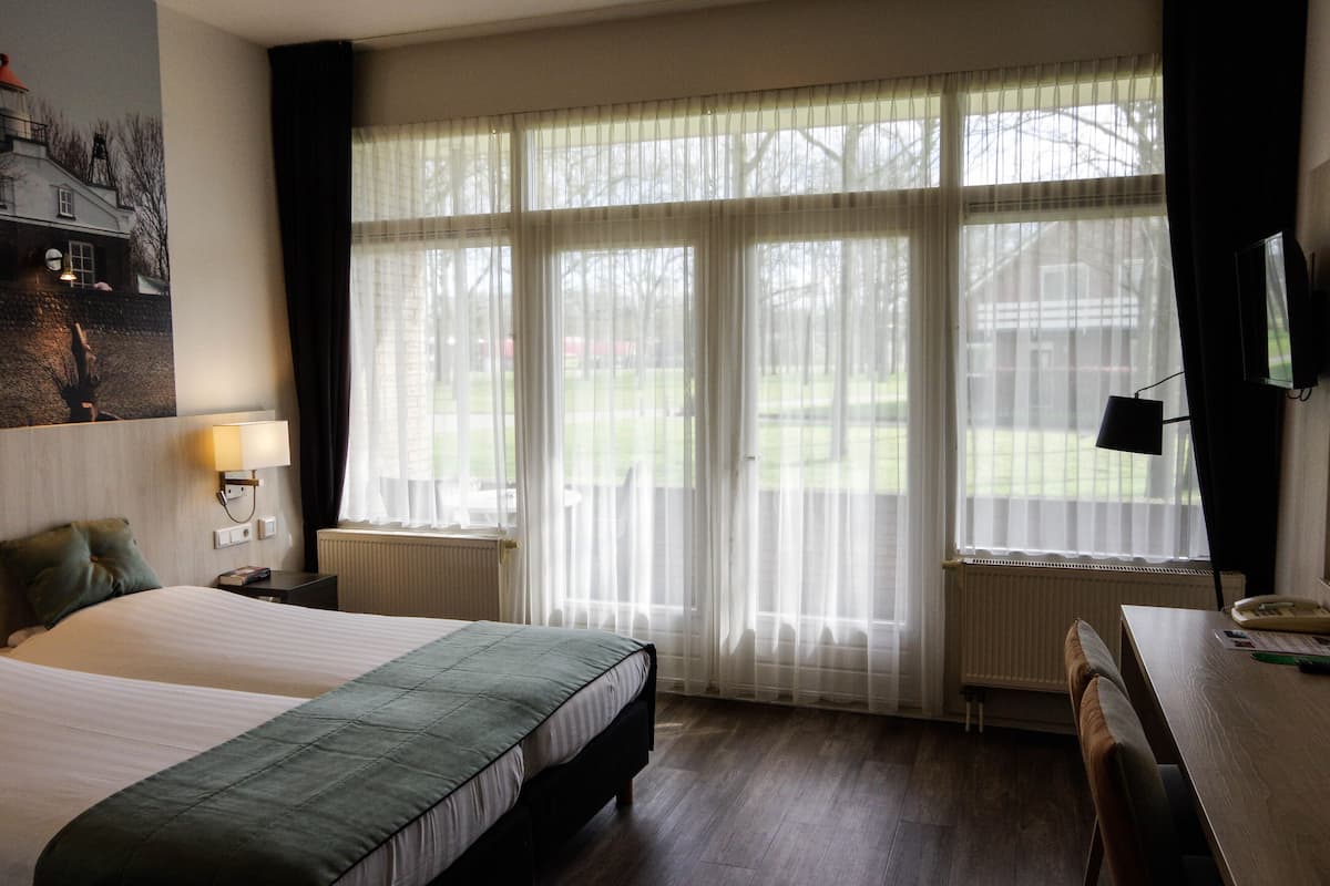Een hotelkamer met twee bedden, een bureau, een stoel, een televisie en een raam met dunne gordijnen.