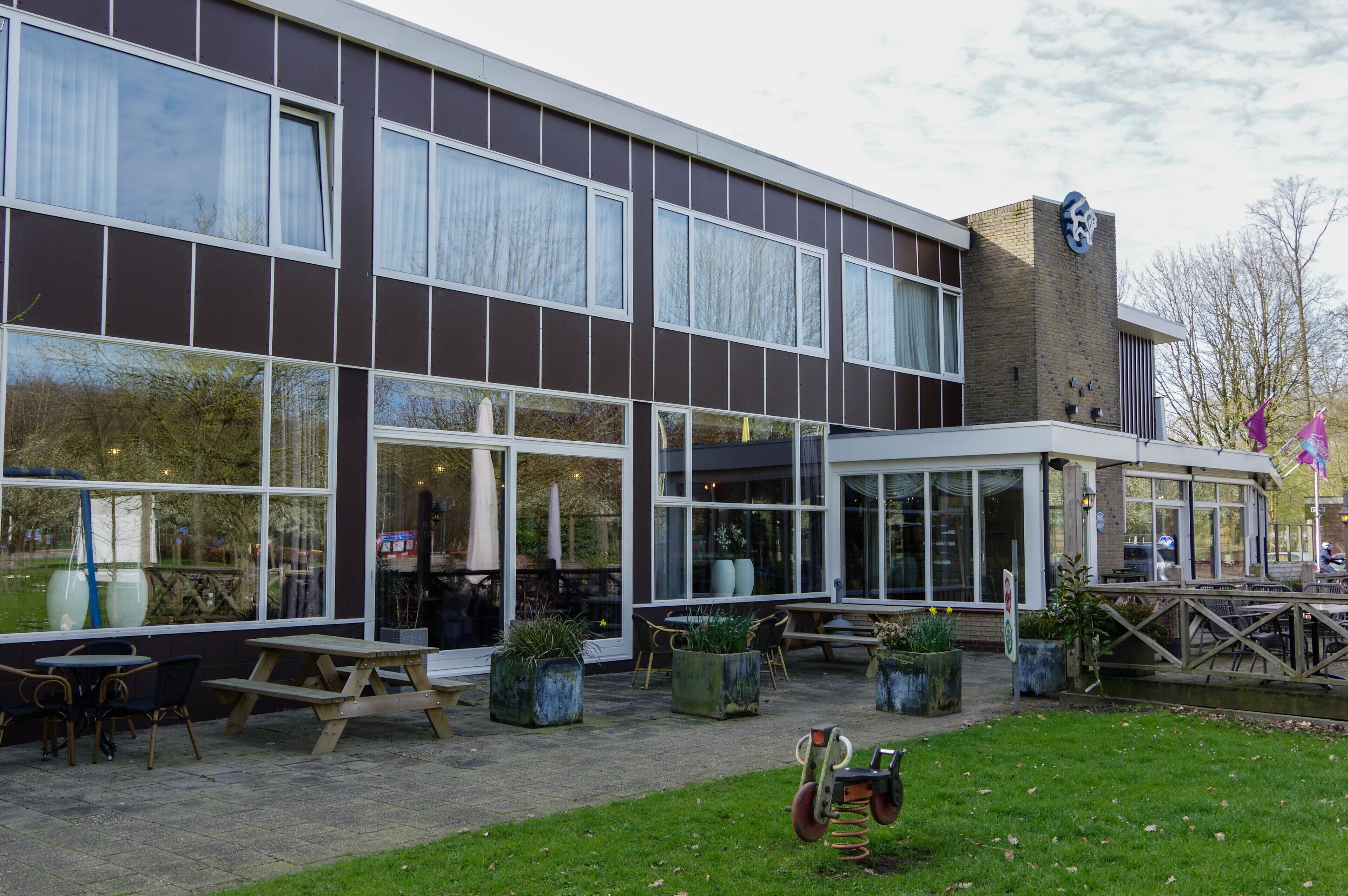 A modern building with large windows, outdoor seating, and a covered patio area.