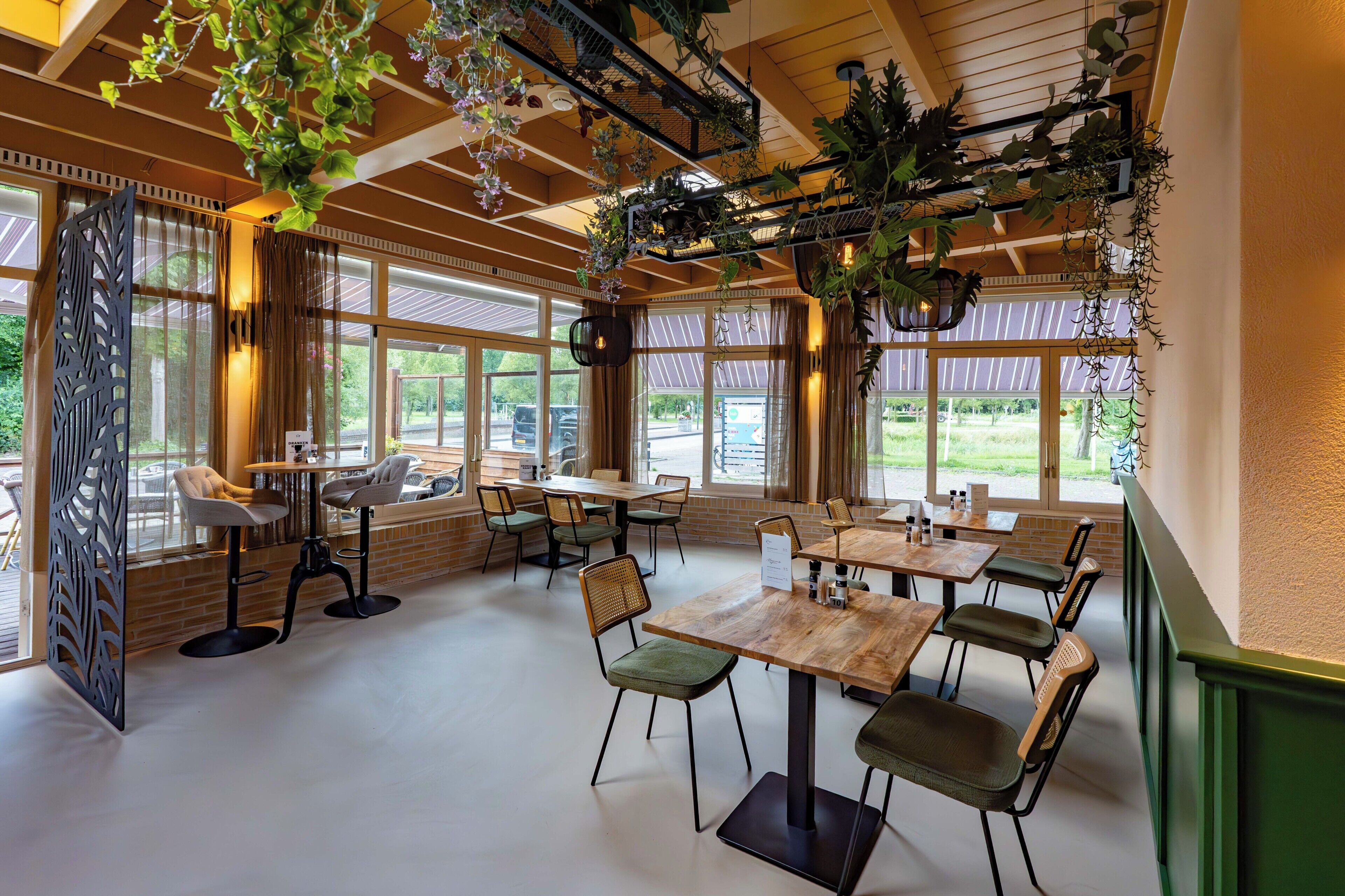 Un restaurant doté de nombreuses tables et chaises, de grandes fenêtres et de plantes suspendues.