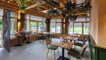 A restaurant with multiple tables and chairs, large windows, and hanging plants.