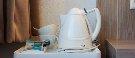 Une chambre d’hôtel équipée d’une machine à café, d’une tasse et d’un plateau contenant un sachet de thé et un petit pot de crème liquide.