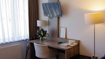 A hotel room with a desk, chair, television, lamp, and a vase with flowers.