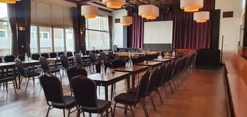 Un salón de conferencias con largas mesas, sillas y una pantalla grande.