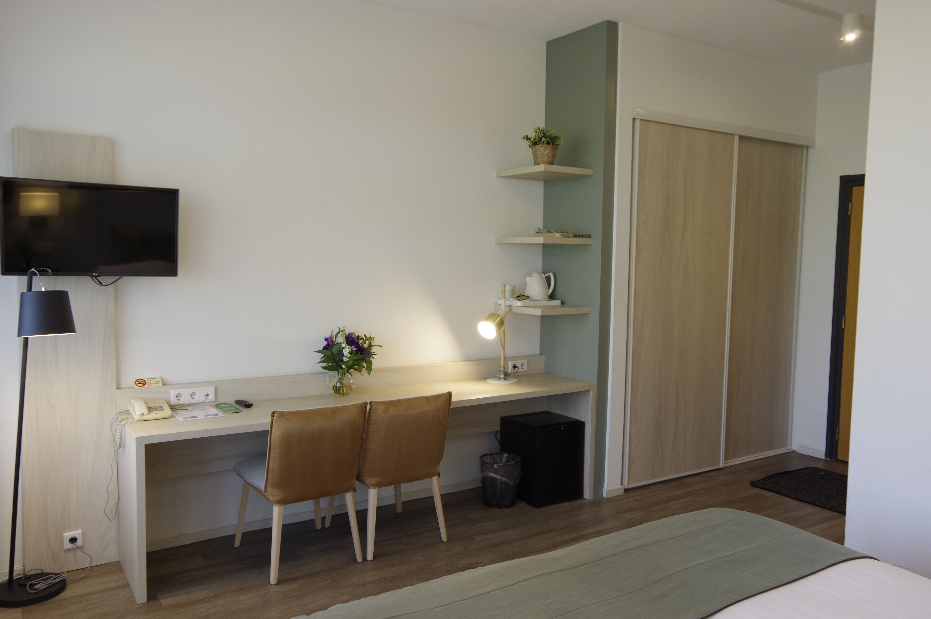 Een moderne slaapkamer met een bed, een bureau met twee stoelen, een televisie en een kledingkast.