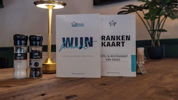 A wooden table with a lamp, two bottles of seasoning, and two informational cards from Hotel van Saaze.