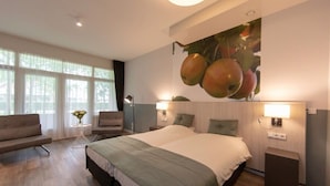 Une chambre d’hôtel moderne dotée d’un grand lit, d’un coin salon avec un canapé et des fauteuils, d’une petite table avec un vase et d’un luminaire fixé au mur.