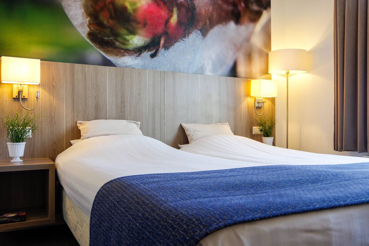 Een hotelkamer met een groot bed, twee bedlampen en een aan de muur bevestigde televisie.