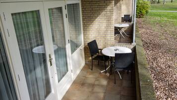 A patio area with a brick wall, a glass door, and a small table with two chairs.