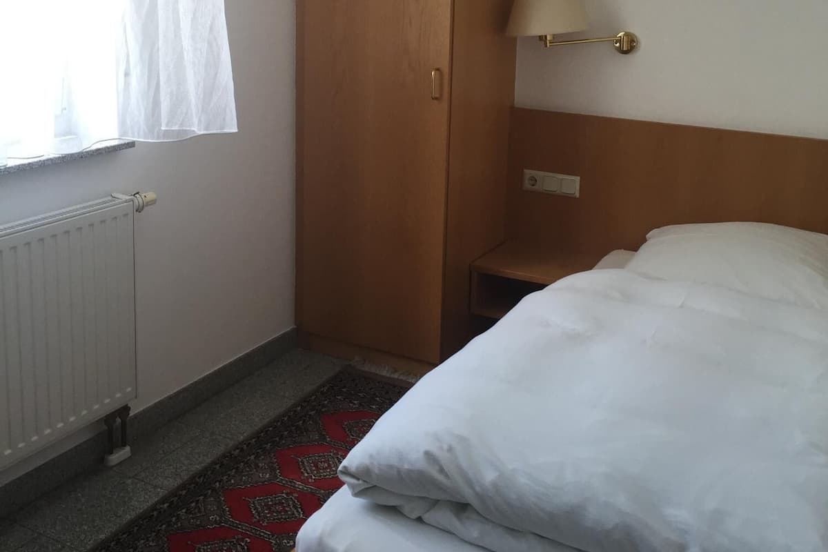 Ein Hotelzimmer mit Holzschrank, Nachttischlampe, Heizkörper und einem gemusterten Teppich.