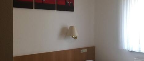 Habitación de hotel con dos camas, una mesita de noche, una lámpara y tres cuadros rojos en la pared.