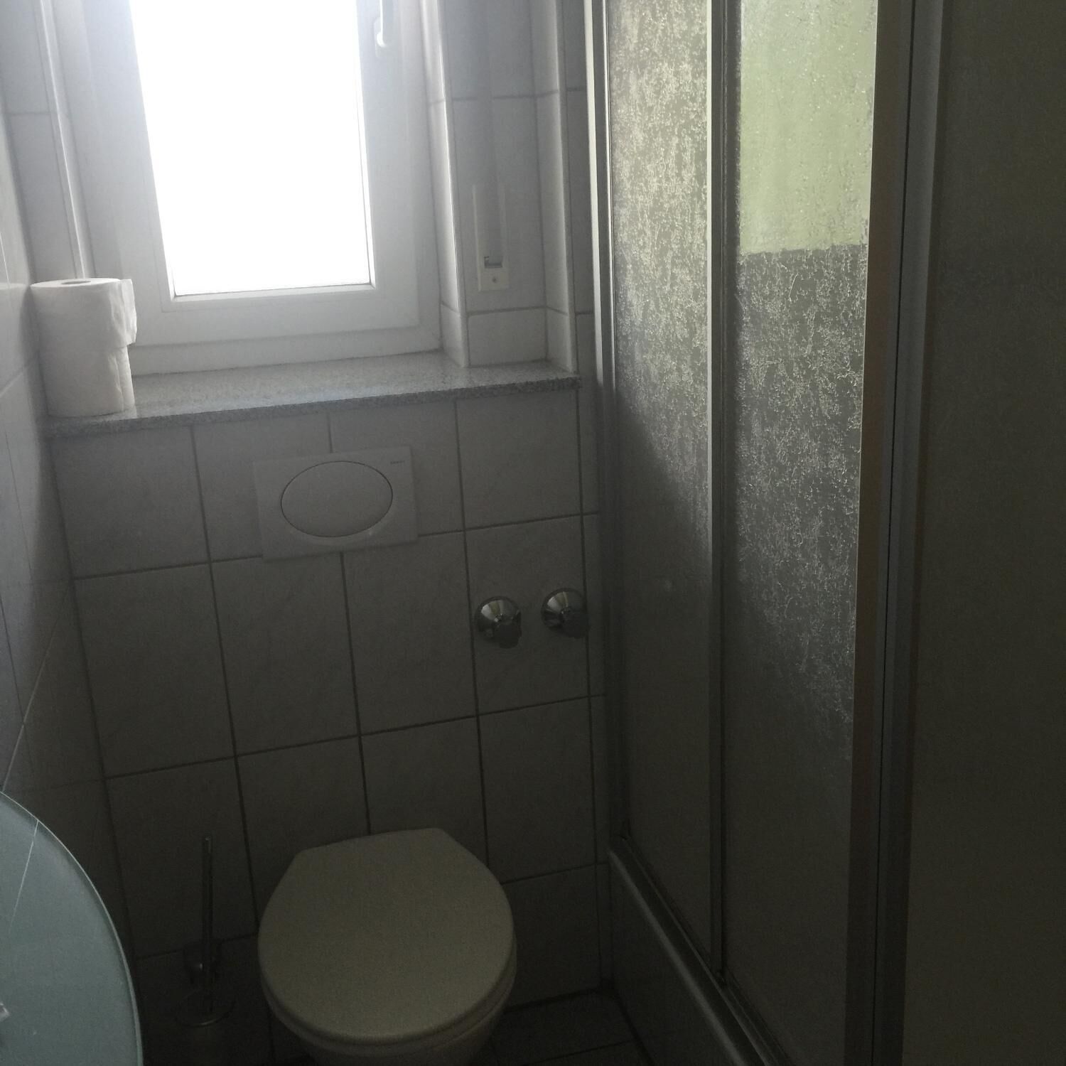 Un baño pequeño y funcional con inodoro, ventana y zona de ducha.