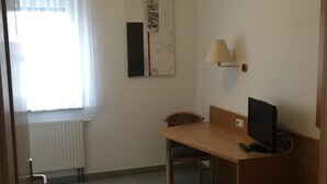 Een kleine kamer met een raam, een bureau, een stoel, een lamp en een bed.