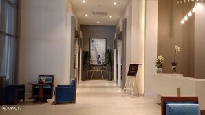 Zona de recepción de un hotel con mostrador, área de descanso con sillas y un pasillo que conduce a una habitación.