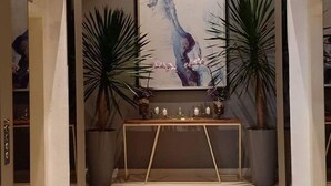 Un pasillo con un cuadro abstracto grande en la pared, dos plantas en macetas y una pequeña mesa con adornos.