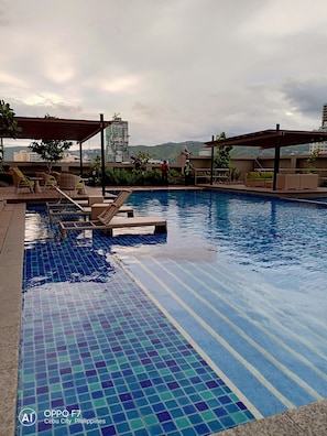 A swimming pool with tiled flooring, lounge chairs, and umbrellas. - Coleen's Bedsit at Horizons 101 (Cebu City)