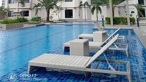 Un moderno edificio de gran altura con piscina, sillones de exterior y palmeras.