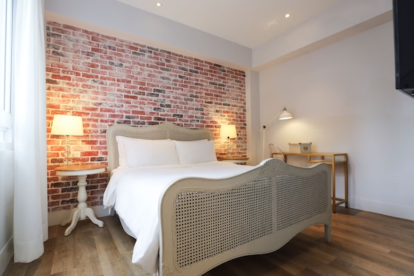 A bedroom with a brick wall, a white bed, two bedside tables with lamps, and a wooden nightstand.