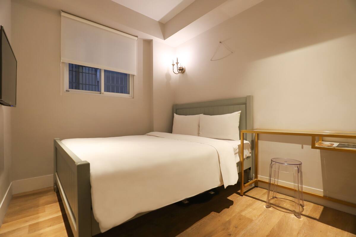 A bedroom with a bed, a window, a nightstand, and a chair.
