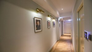 A hallway with framed pictures on the wall, a wooden floor, and a door with a digital display. - Slow Town Hotel - Reel (Taipei)