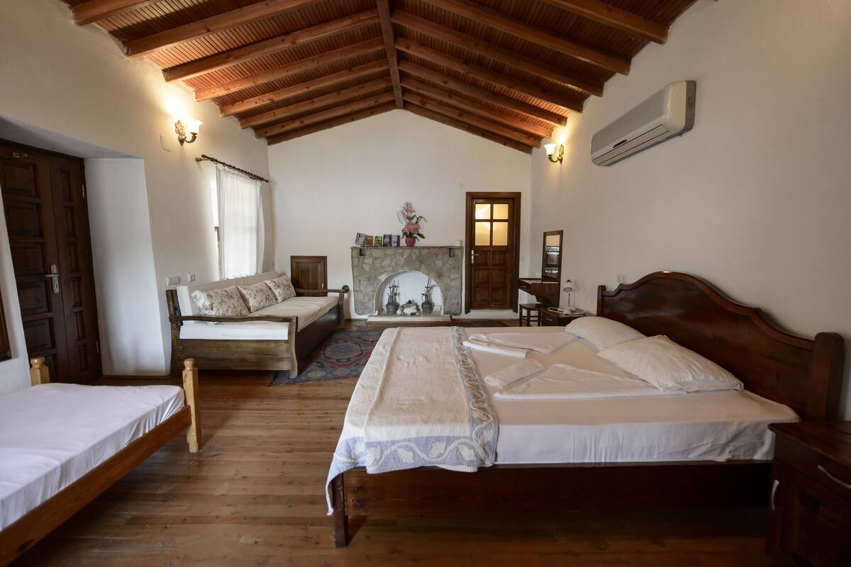 A bedroom with a wooden ceiling, a fireplace, a bed, a sofa, and a wooden floor.