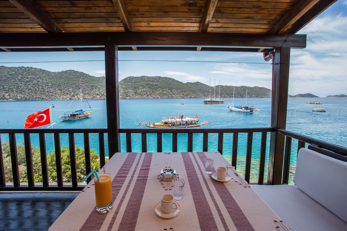 A table set with a drink, glasses, and a flag on a balcony overlooking a body of water with boats.