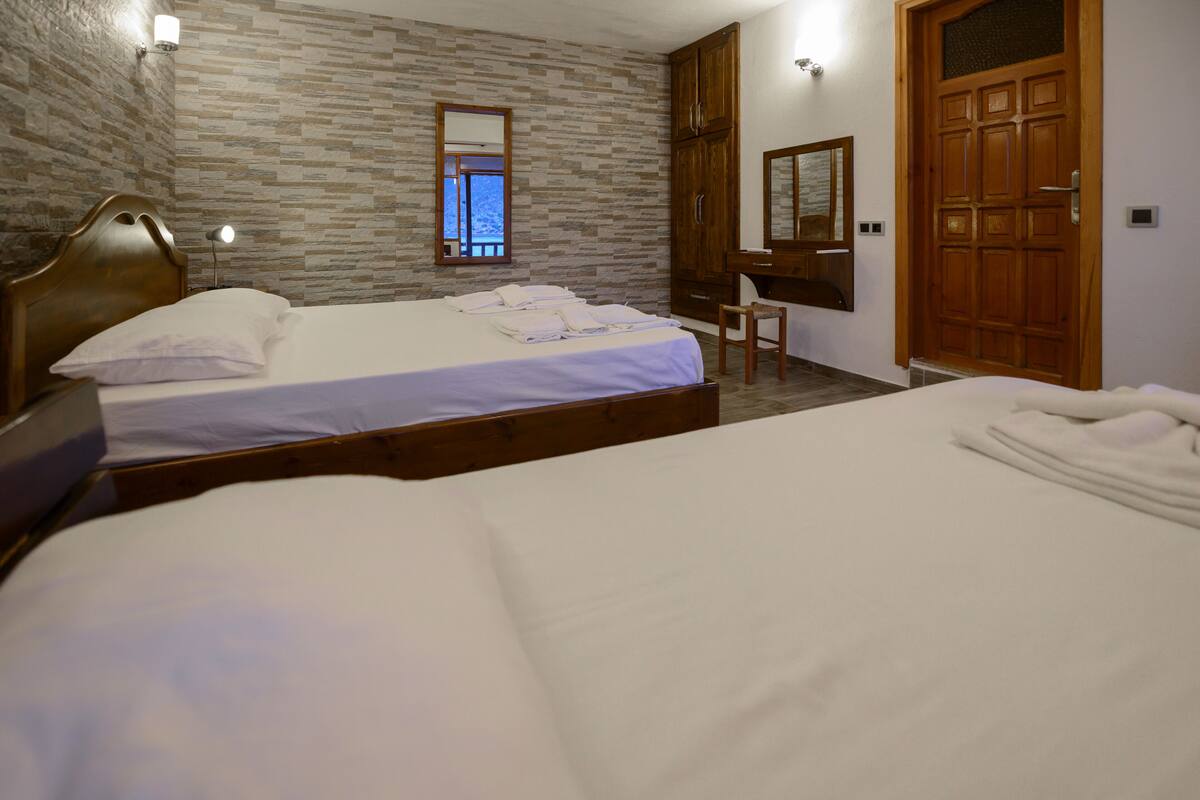 A bedroom with two beds, a wooden wardrobe, a desk, and a mirror.