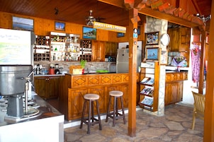 Un accogliente bar in stile baita, con interni in legno, pavimento in pietra e un bancone con sgabelli.