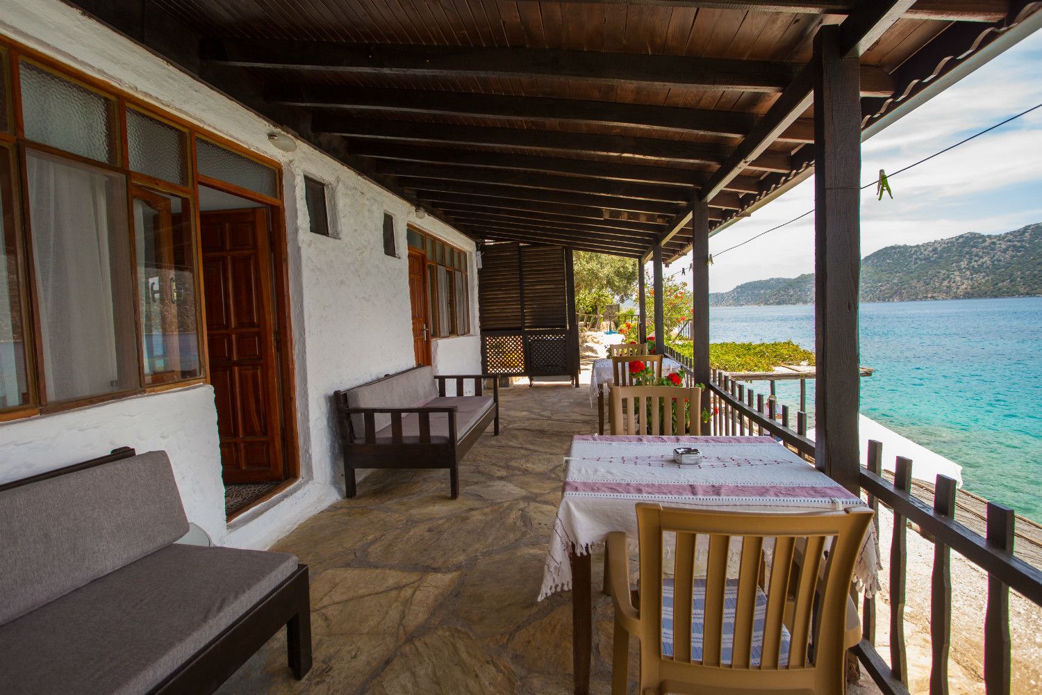 Un área de estar al aire libre techada con suelo de piedra, muebles de madera y vista al mar.