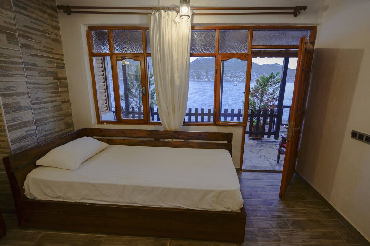 A bedroom with a wooden bed, a view of a lake through large windows, and a stone wall.