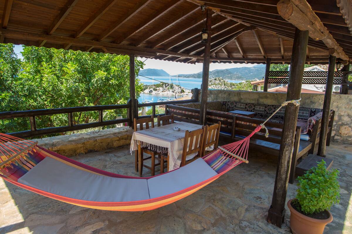 A covered outdoor seating area with a table and chairs, a hammock, and a potted plant.