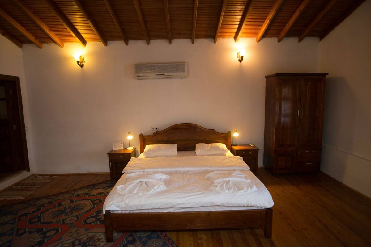 A bedroom with a wooden bed, two bedside tables with lamps, a wardrobe, and a patterned rug.