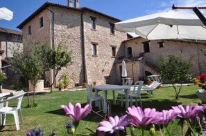 Un edificio de piedra con un patio, mobiliario exterior y un gran paraguas.