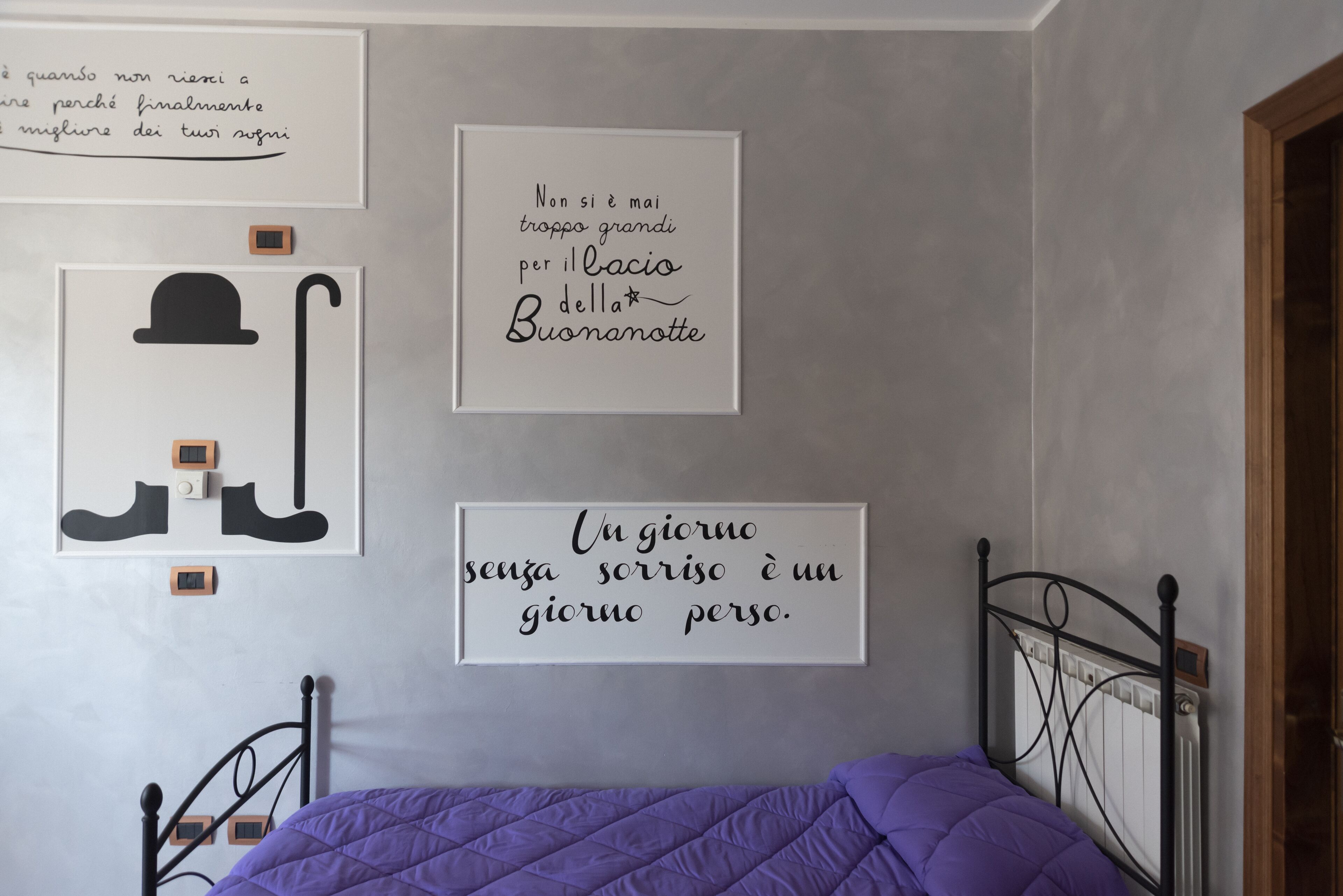 A bedroom with a bed, a wall with framed motivational quotes, and a radiator.