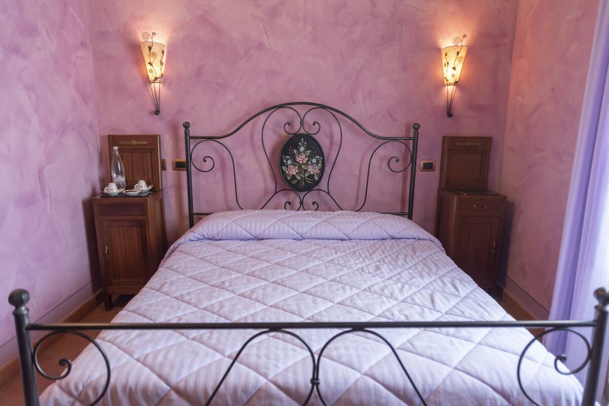 Un lit avec un matelas matelassé, deux tables de chevet ornées d’objets décoratifs et des appliques murales.